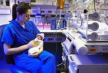 Krankenschwester mit Frühgeborenem auf dem Arm vor Inkubator, ©Corbis