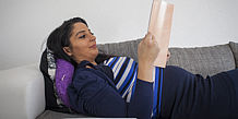 schwangere Frau liegt lesend auf dem Sofa