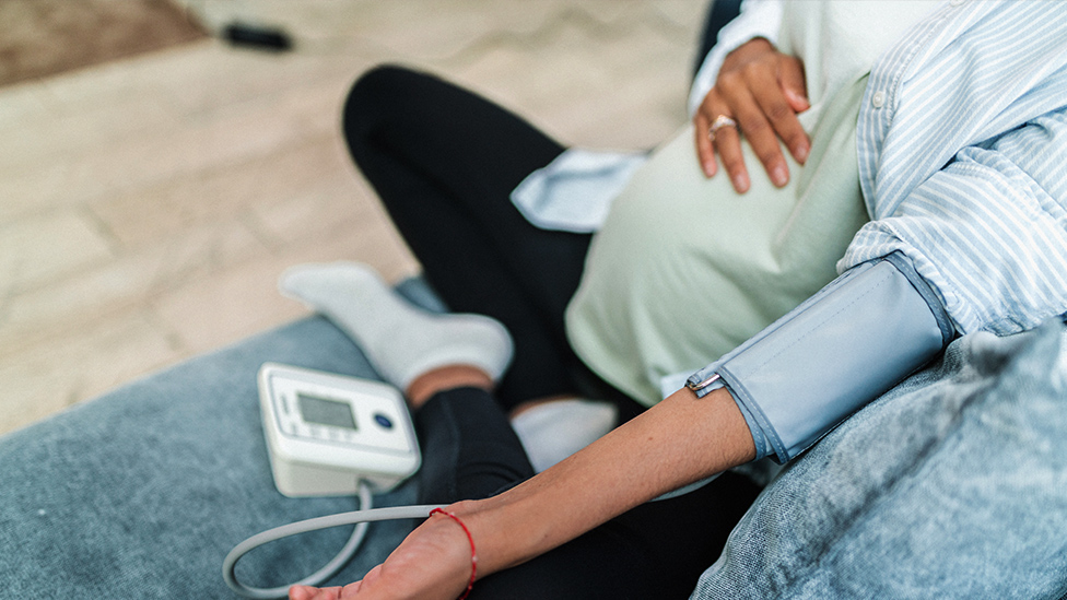 Schwangere Frau beim Blutdruckmessen auf dem Sofa