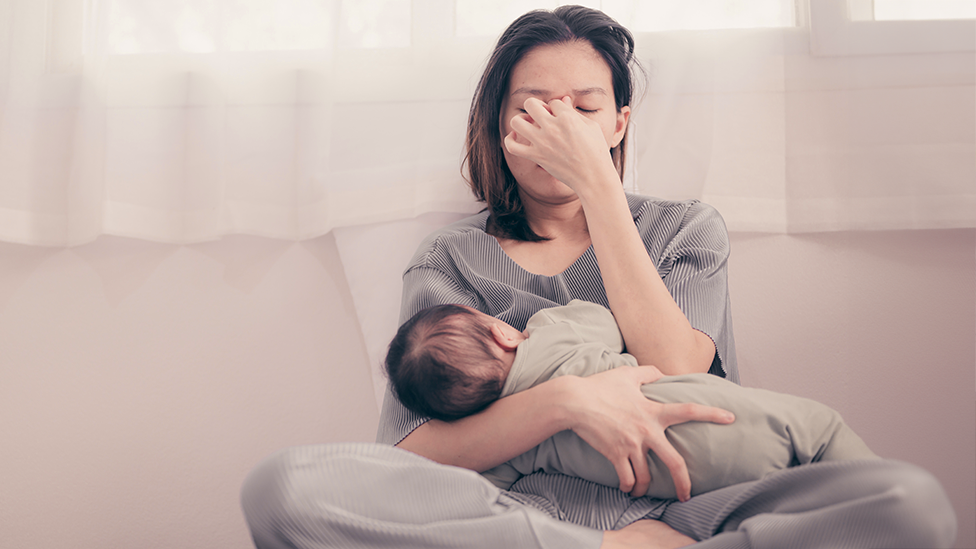 Erschöpfte Mutter stillt Baby im Wochenbett